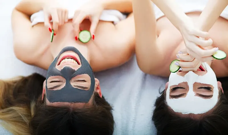 Home spa. Two women holding pieces of cucumber on their faces lying the bed. 