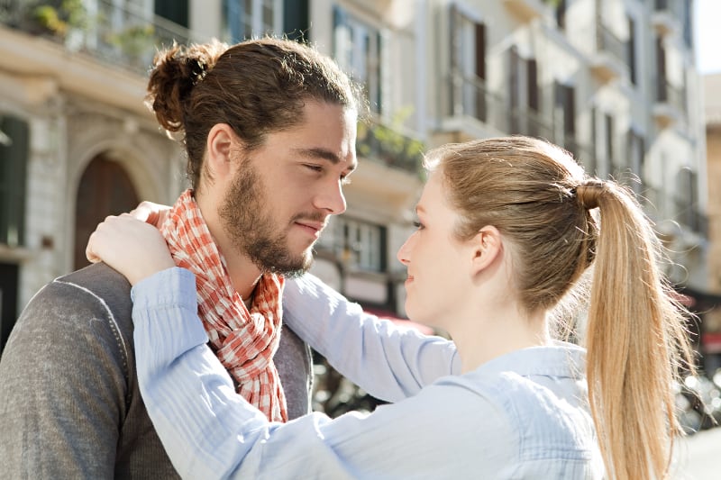 side view of smiling couple hugging and looking each other outside