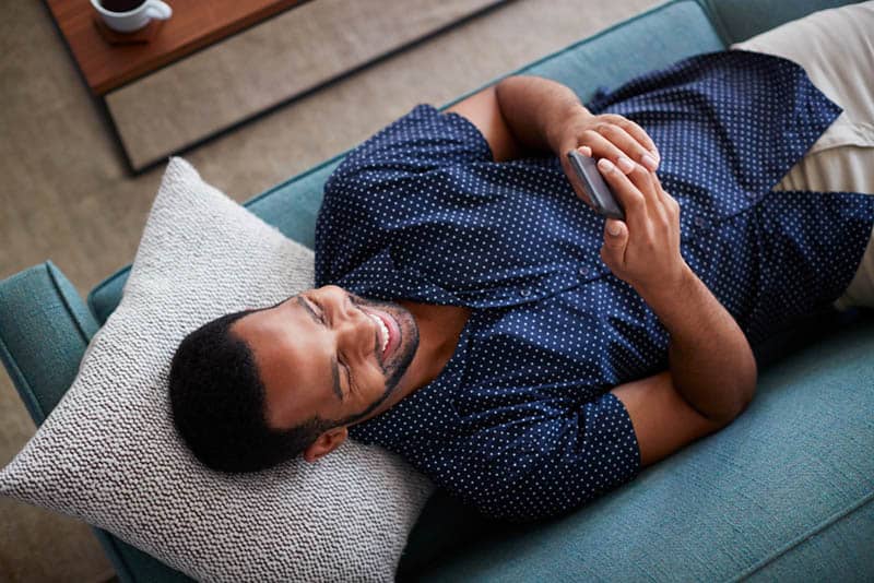 hombre sonriente escribiendo en su teléfono en casa