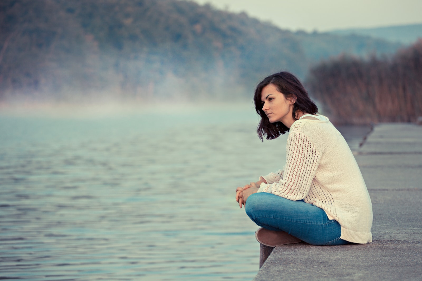 the woman sits pensively beside the pier