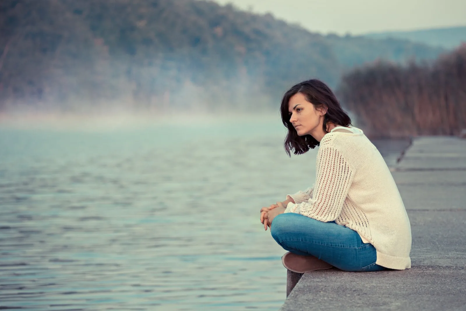 the woman sits pensively beside the pier