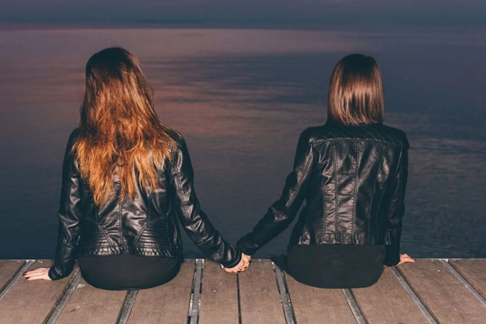 two friends are sitting next to the pier holding hands