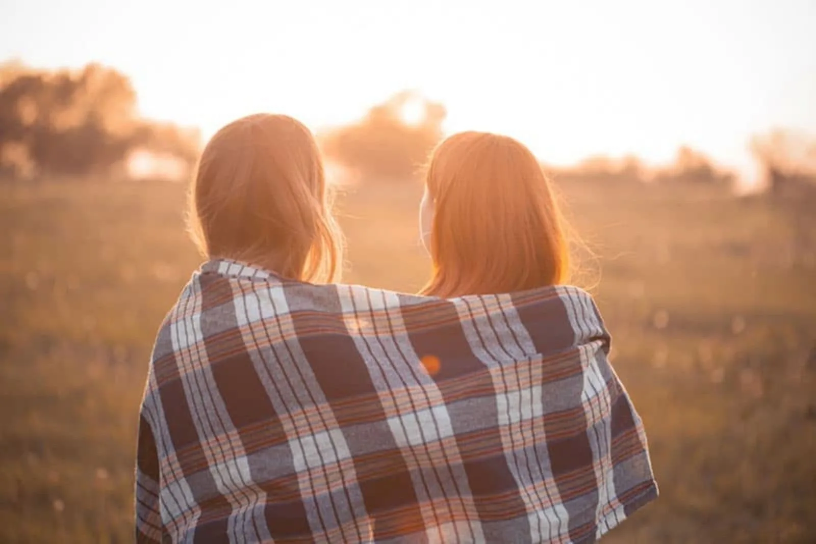 two friends standing embracing covered themselves with a blanket