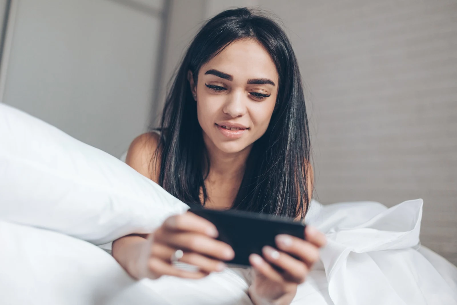woman using smartphone while lying on her bed