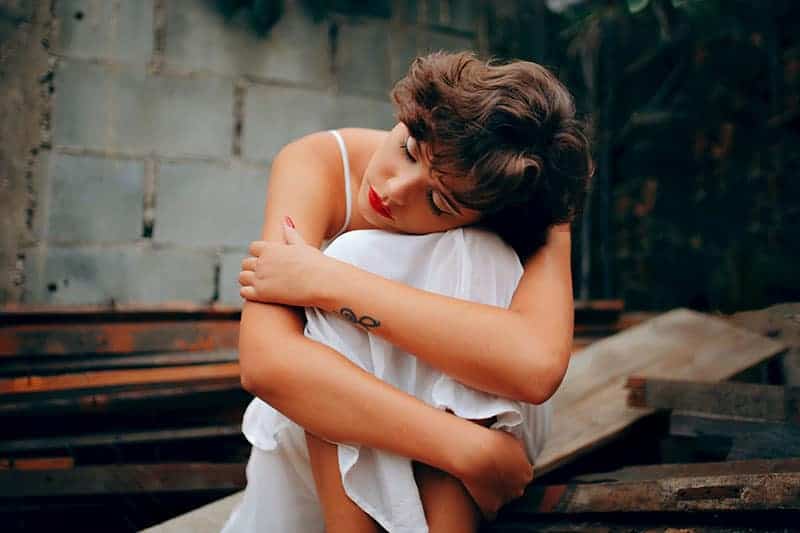 woman wearing white dress leaning on her knee closed eyes