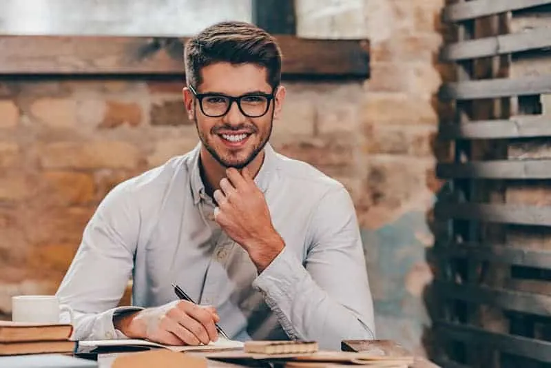 young man wearing eyeglasses while holding a pen