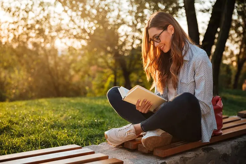 young woman reading a book on the bench