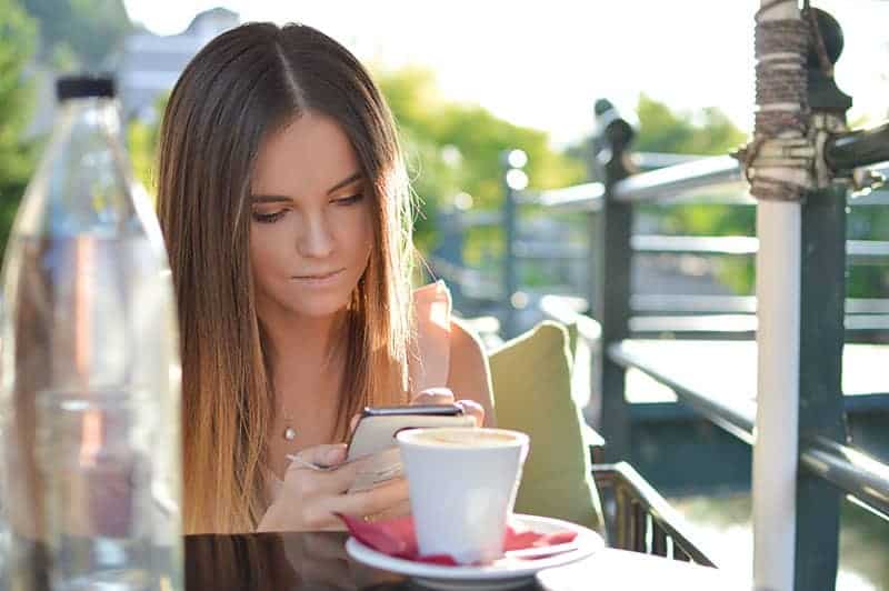 mulher jovem a escrever no telemóvel num café de rua