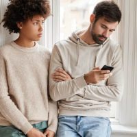 man typing on his phone while woman watching him thoughtfully