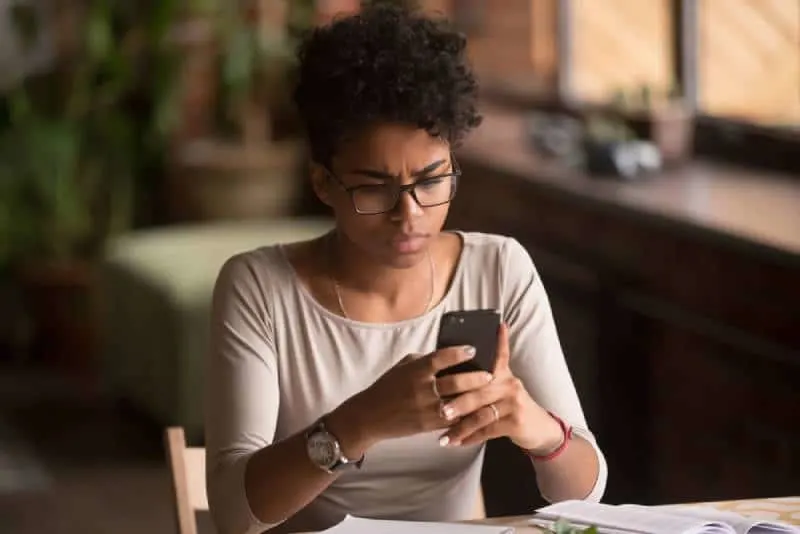Angry confused african woman holding phone