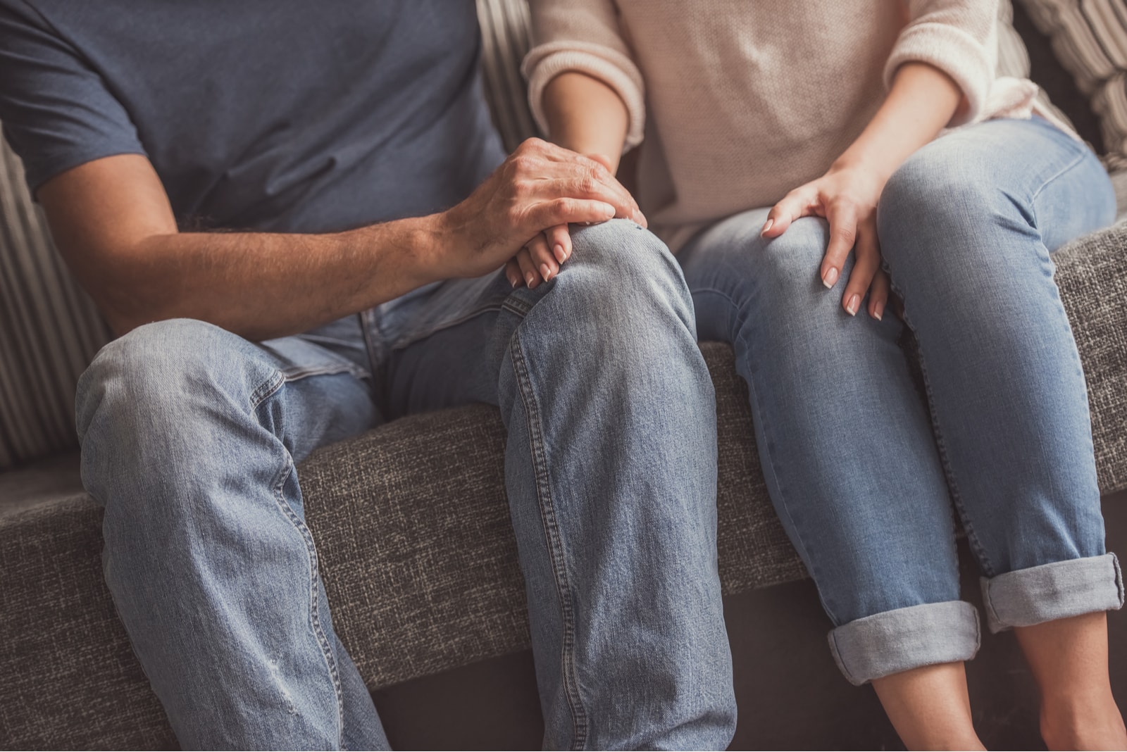 Cropped image of beautiful couple holding hands while resting on couch at home