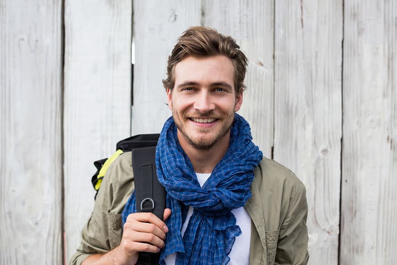 Happy young man carrying backpack outdoors