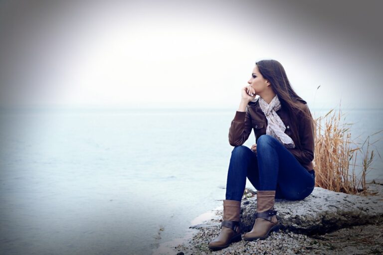 pensive woman wearing jacket sitting on the rock
