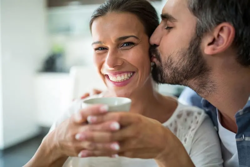 Man kissing woman on cheeks while having coffee at home