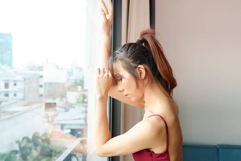 Triste e stanca donna transgender asiatica che guarda attraverso la finestra della scuola di danza dopo l'allenamento