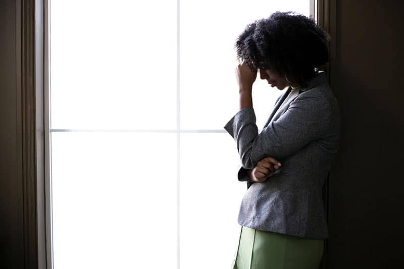 Silhouette di una donna d'affari afroamericana di colore, stressata e preoccupata, che pensa a problemi e fallimenti vicino alla finestra dell'ufficio. Sembra depressa o turbata da debiti o fallimenti.