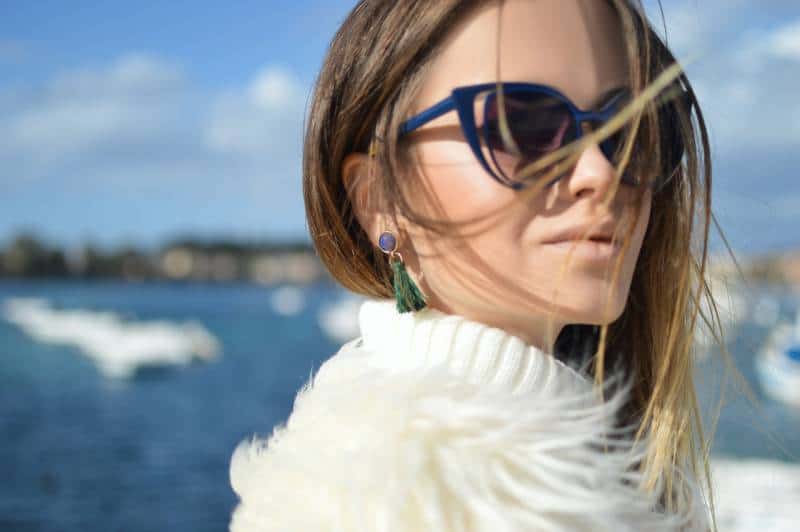 Woman wearing blue framed cat eye sunglasses with water in background