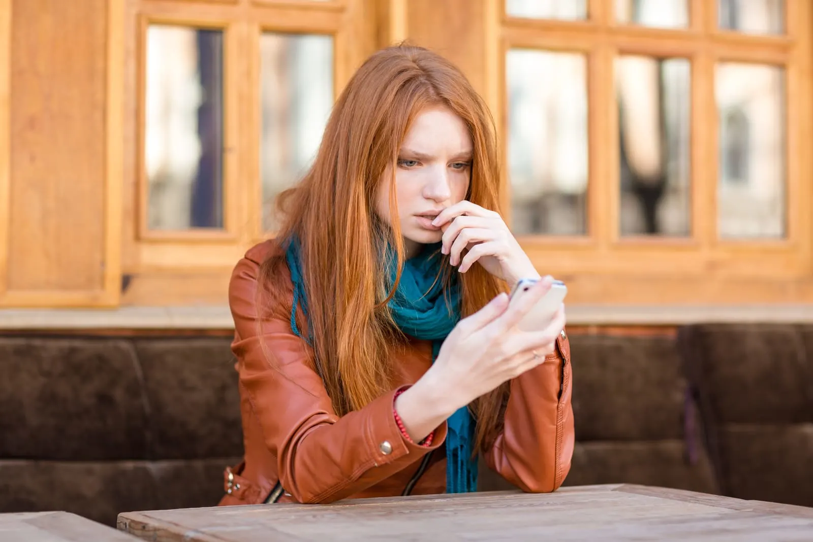 a woman with long red hair is sitting at a table with a phone in her hand