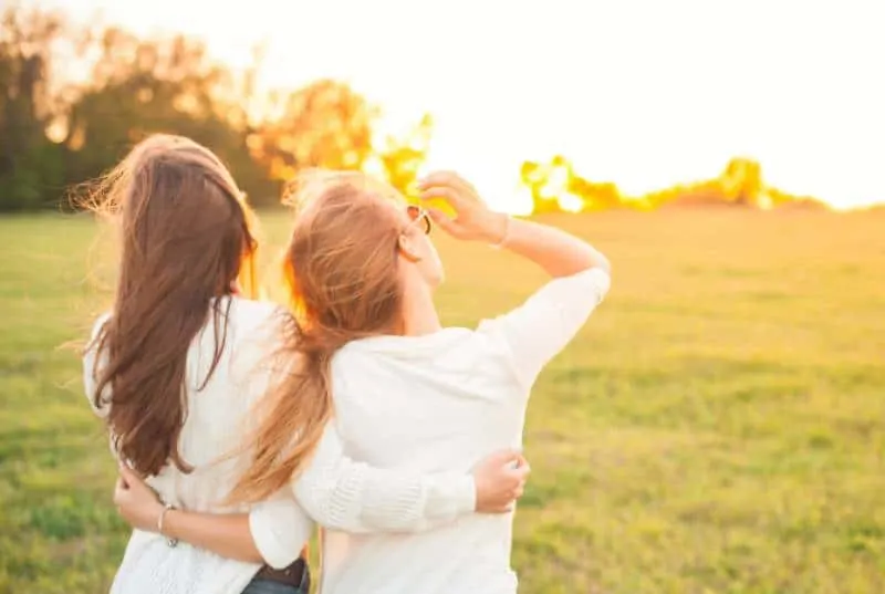back view of female friends on grass field during sunset