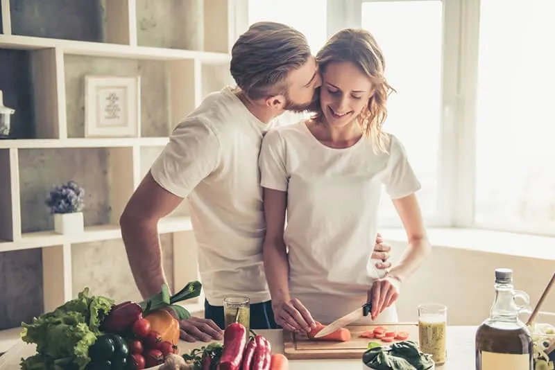 couple is talking and smiling while cooking food in kitchen