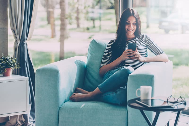 happy woman sitting on sofa with phone