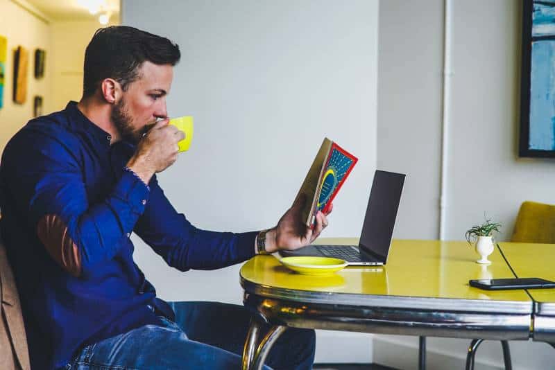 uomo che beve su una tazza gialla mentre legge un libro