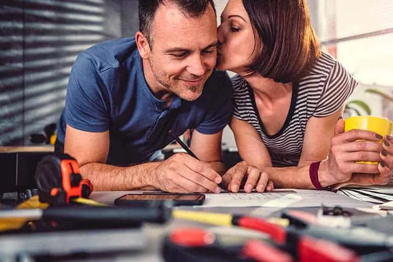 man holding a pen and writing while woman kisses him on cheek