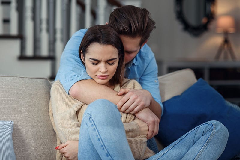 man hugging sad woman on the couch