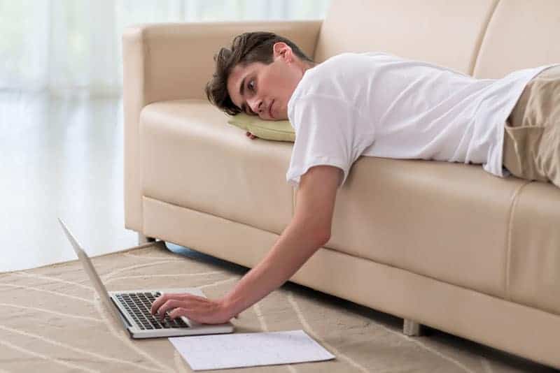 man lying on couch and typing on laptop