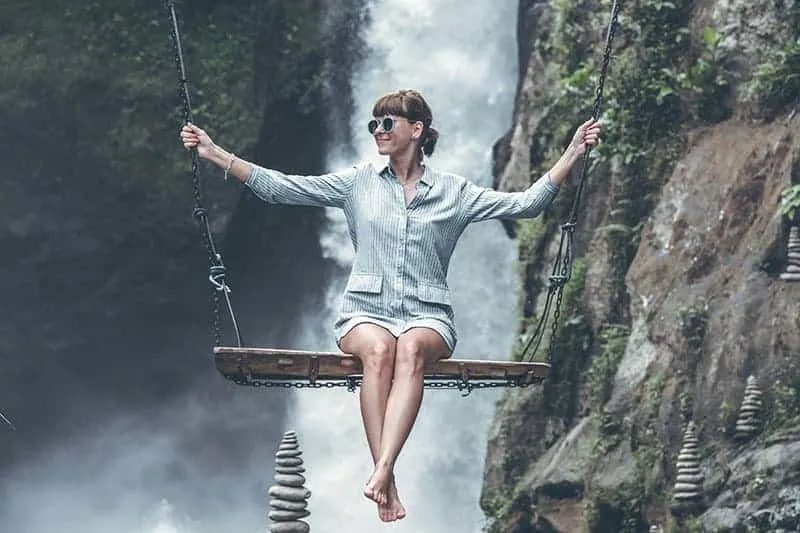 photo of woman riding swing in front of waterfalls