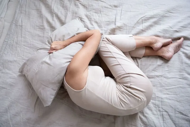 sad woman lying on bed with head covered with pillow