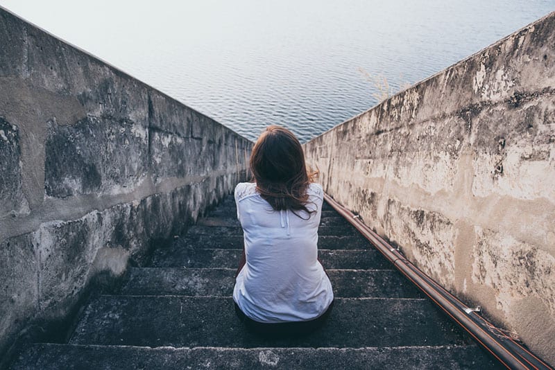 sad woman sitting on the stairs and looking at sea