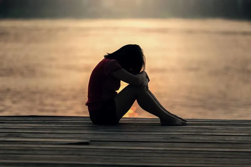 sad young woman sitting by the lake