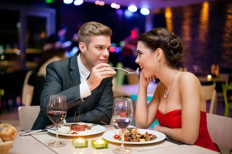 Affectionate couple in restaurant, him feeding she