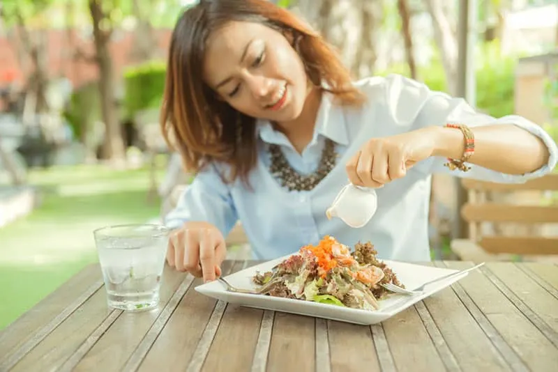 Asian woman and her happiness When eating salad Resting on a plate In the middle of the green garden,Focus on the hand