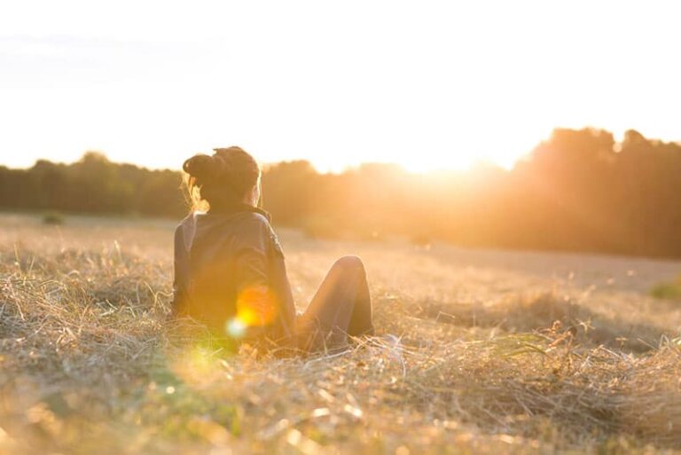 Retrato de una hermosa mujer joven o niña en el prado viendo la puesta de sol disfrutando de la naturaleza la noche de verano al aire libre. Suave luz roja. Luz del sol.