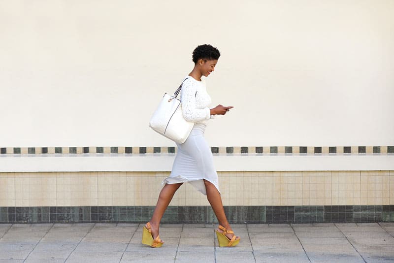Ritratto laterale a figura intera di una giovane donna che cammina e invia messaggi di testo al cellulare