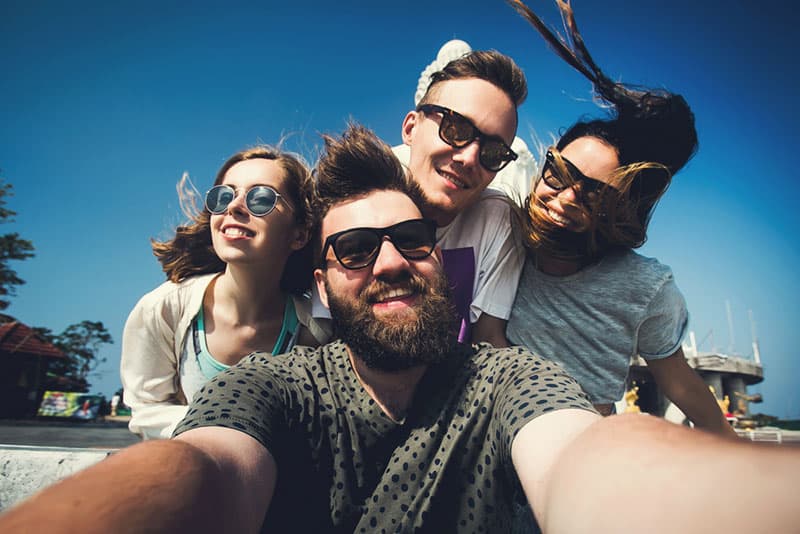 Grupo multirracial de jovens amigos hipster tiram uma fotografia selfie com a câmara do smartphone em Phuket enquanto viajam pela Tailândia em férias. Atividade divertida ao ar livre de jovens estudantes fora de casa.