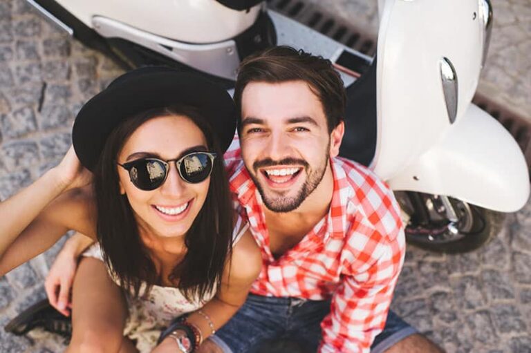 Close up fashion portrait of stylish young couple pretty woman and handsome man posing near a vintage scooter on a summer day