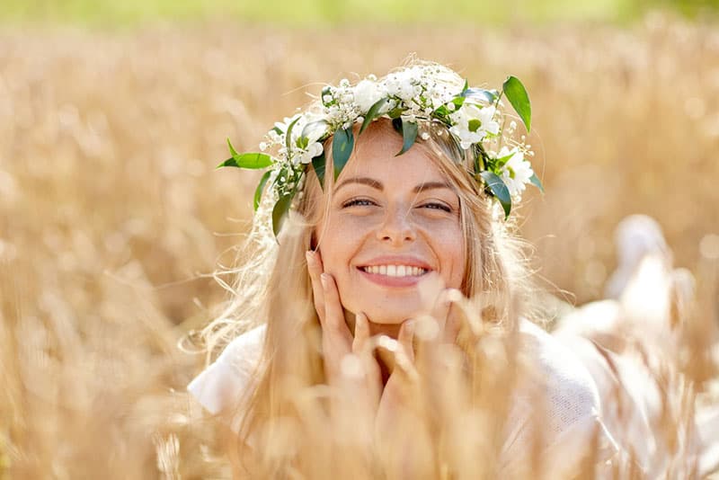 naturaleza, vacaciones de verano, las vacaciones y el concepto de la gente - cara de la mujer sonriente feliz o adolescente n en corona de flores en el campo de cereales