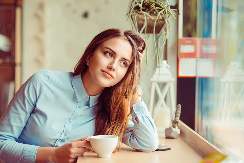 Soñando despierta en una pausa para el café. Pensive mujer feliz recordando mirando de reojo sentado en un bar, cafetería bebiendo té.