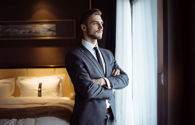 Young handsome man relaxing at his apartment in a hotel after business meeting. Business trip. Booking hotel during your vacation. Businessman in luxury room of the expensive beautiful hotel.