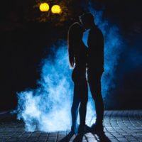 El hombre y la mujer besándose en la calle sobre un fondo de humo azul. noche