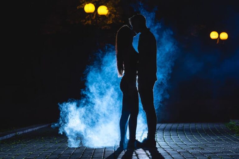 El hombre y la mujer besándose en la calle sobre un fondo de humo azul. noche