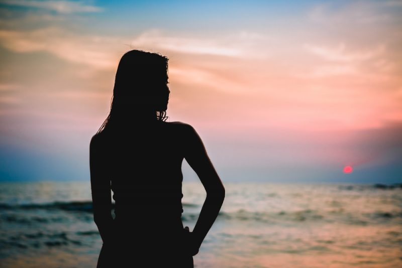 silhouette of young woman staring into the sea.