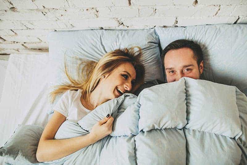 smiling couple laying on bed covered with blanket