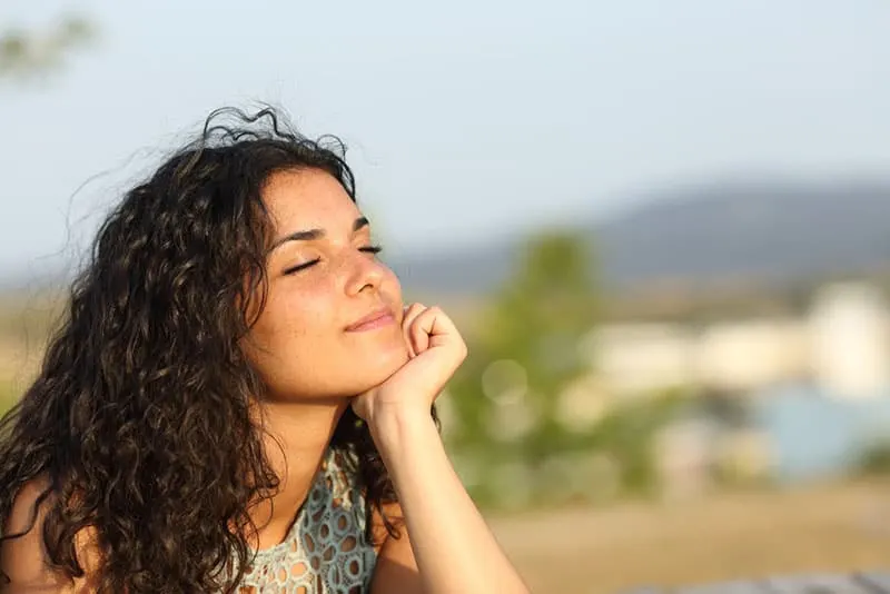 smiling woman standing outdoor with closed eyes