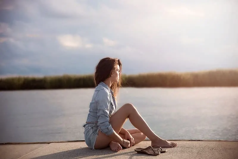 thoughtful woman sitting on dock beside water