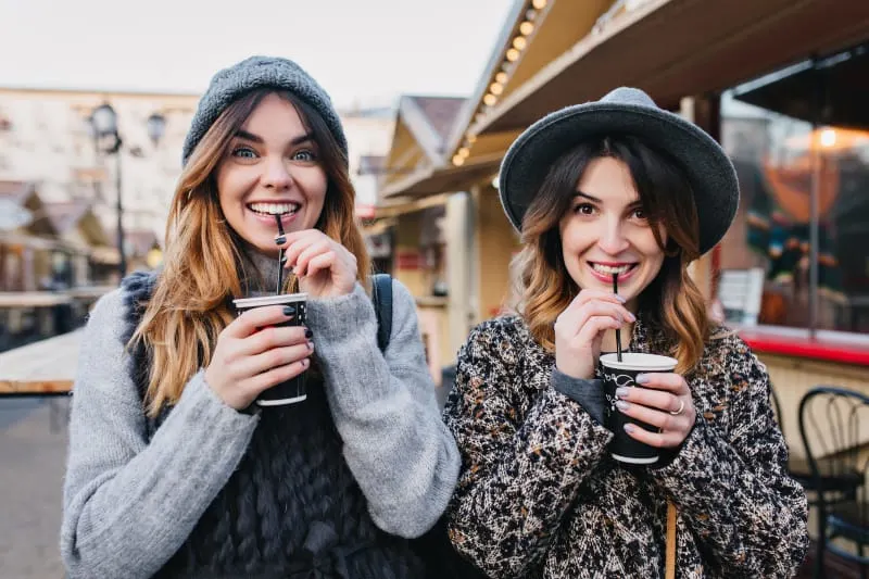 two female friends standing to each other and drinking coffee from cup