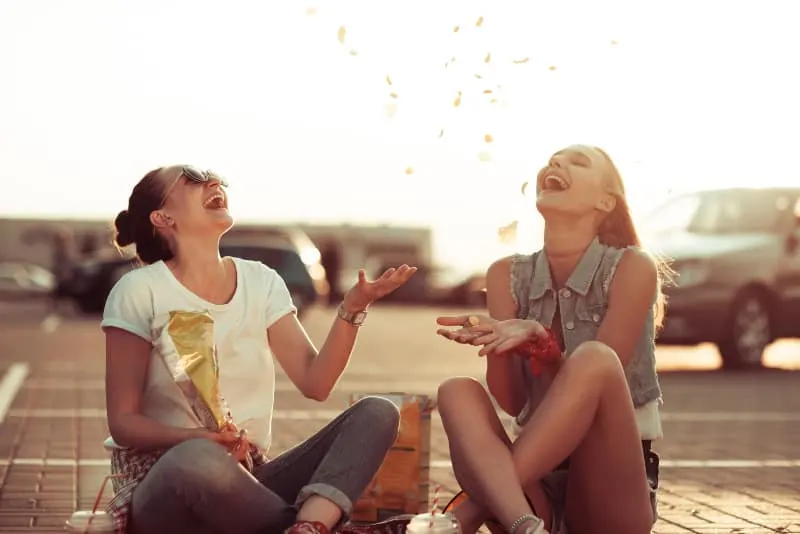 two smiling female friends eating chips outside